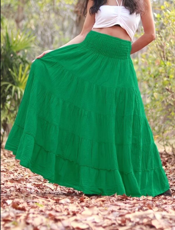 woman wearing green boho skirt and a white top, a forest in the background