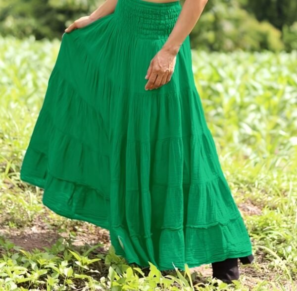 woman turned to her side wearing green boho skirt and black shoes, grass in the background