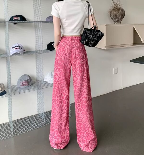 woman turned to her back wearing pink leopard print pants and white top, white room in the background