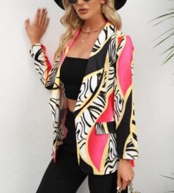 woman wearing stylish colorful blazer, a black top and black pants, she is putting one hand on a white wall behind her