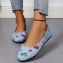 woman wearing colorful patchwork flats, jeans and a black ankle bracelet, she is standing on the grey floor