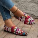 woman wearing pink colorful summer flats and jeans, she is crossing her legs on the wooden floor