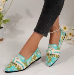 woman wearing multi colored loafers and black jeans, white wall and flowers in the background