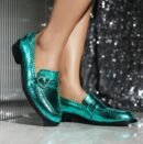 woman wearing shiny colorful loafers, shiny grey wall behind her