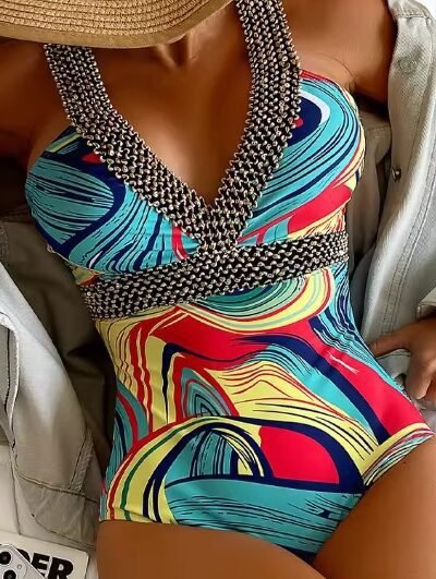 woman wearing color block one piece swimsuit and a beige sun hat, she is sitting on a white blanket