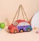 colorful car purse lying on a beige table, colorful macaroons and a green apple next to it