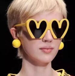 woman with short blonde hair wearing colorful heart shaped sunglasses and yellow earrings