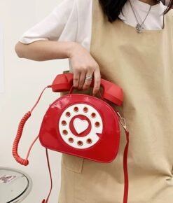 woman wearing a beige dress and holding up the red colorful telephone bag