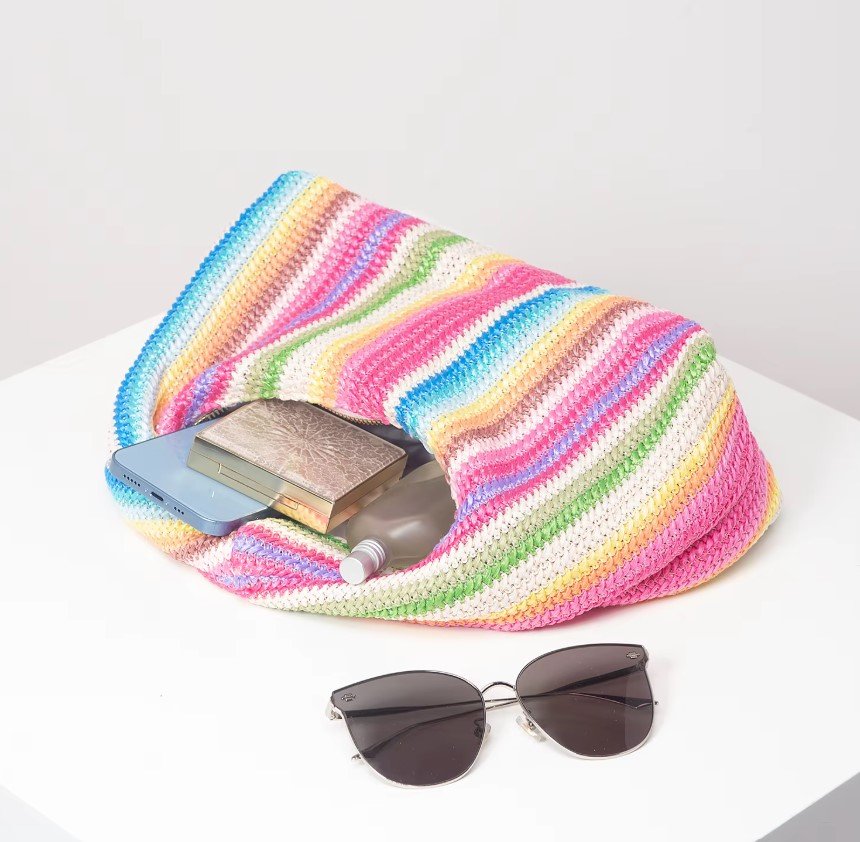 vintage colorful bag filled with a phone, powder, perfume, sunglasses next to it