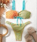 front view of colorful bikini with stripes on the white blanket, flowers and slippers next to it