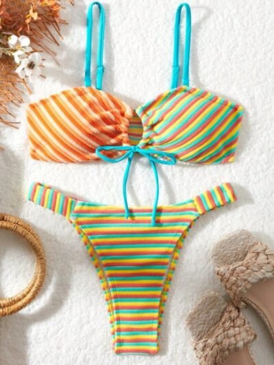 front view of colorful bikini with stripes on the white blanket, flowers and slippers next to it