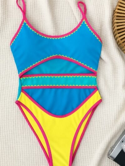 colorful cut out one piece swimsuit lying on a white blanket, a camera next to it