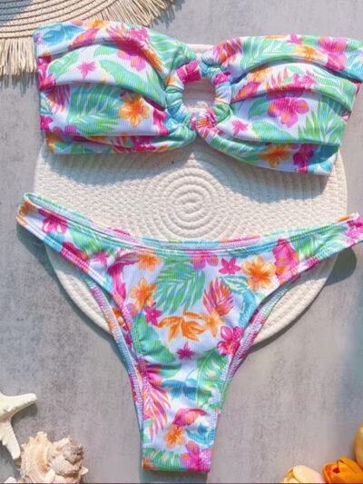 tropical colorful bikini lying on a grey table, surrounded by flowers and seashells