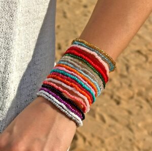 woman wearing colorful bracelets and a grey dress, sand in the background