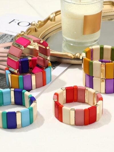 front view of colorful rectangle beads bracelets on a beige table, a candle next to them
