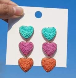 colorful heart-shaped earrings hung on a white paper, sky in the background