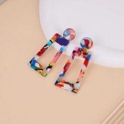 large colorful earrings on a beige surface, white plate under them