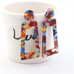 side view of large colorful earrings hung on a white coffee cup