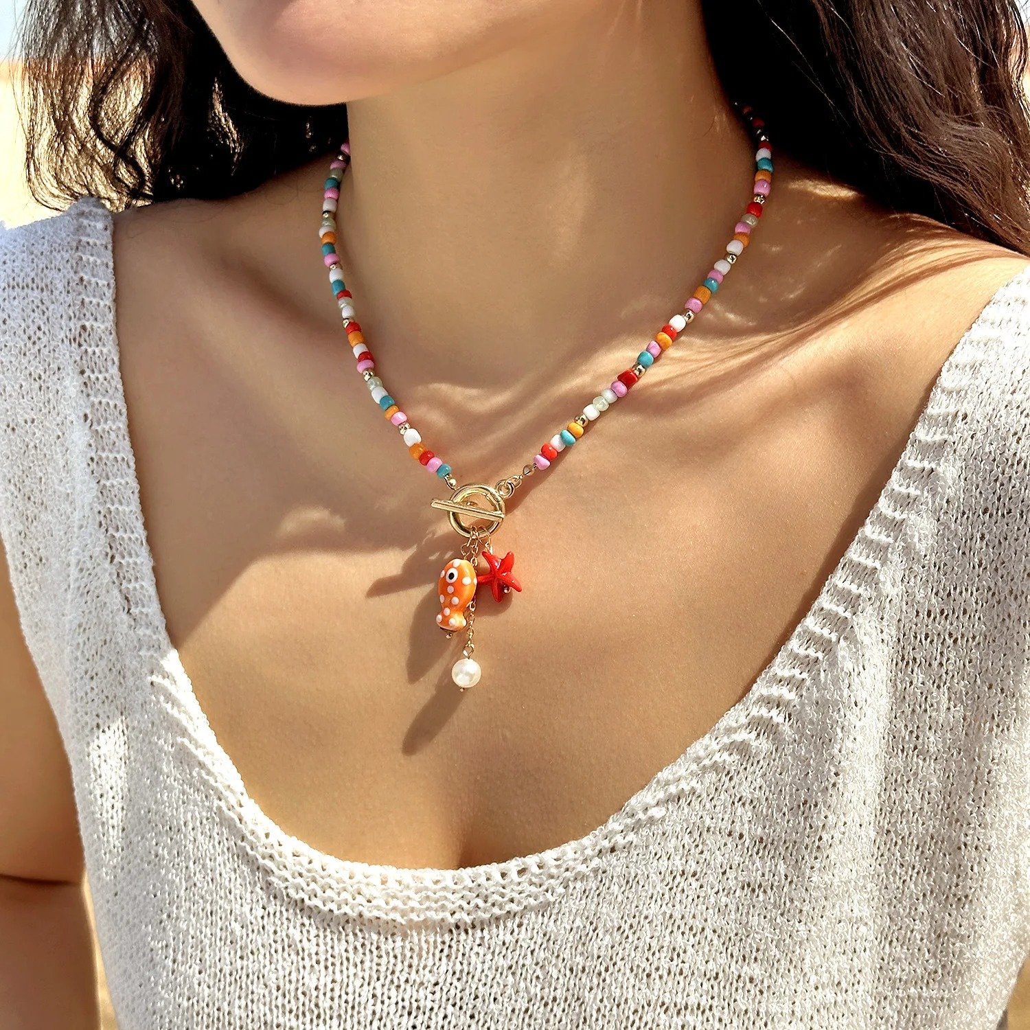 woman with brown hair wearing colorful sea-inspired necklace and a beige sweather